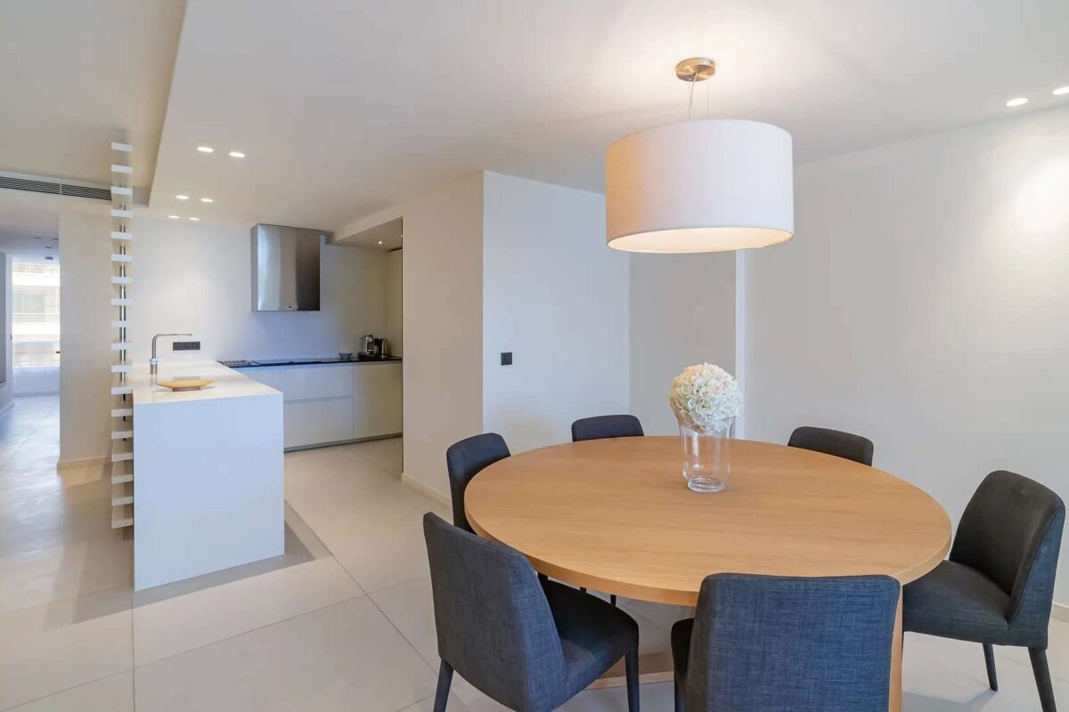 Bright, modern open-plan kitchen and dining room. Features a round wood table, grey chairs, white kitchen island, and contemporary lighting.