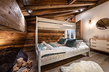 Cozy cabin bedroom with rustic wood-paneled walls, a white wooden bunk bed, a fluffy white rug, and a slanted ceiling.