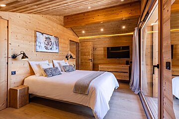 A cozy, wood-paneled chalet bedroom featuring a large white bed with leopard-print accent pillows and warm, ambient lighting.