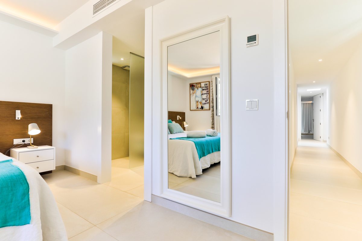A bedroom with a full length mirror and a thermostat on the wall
