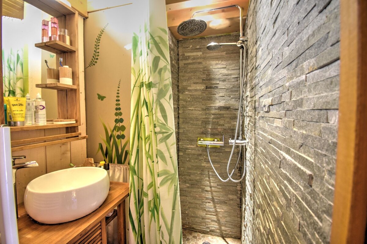 Rustic bathroom featuring a white bowl sink on a wooden vanity and a shower with stone tile walls and a green bamboo-patterned curtain.