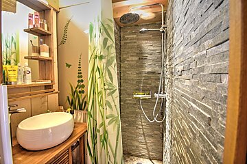 Rustic bathroom featuring a white bowl sink on a wooden vanity and a shower with stone tile walls and a green bamboo-patterned curtain.