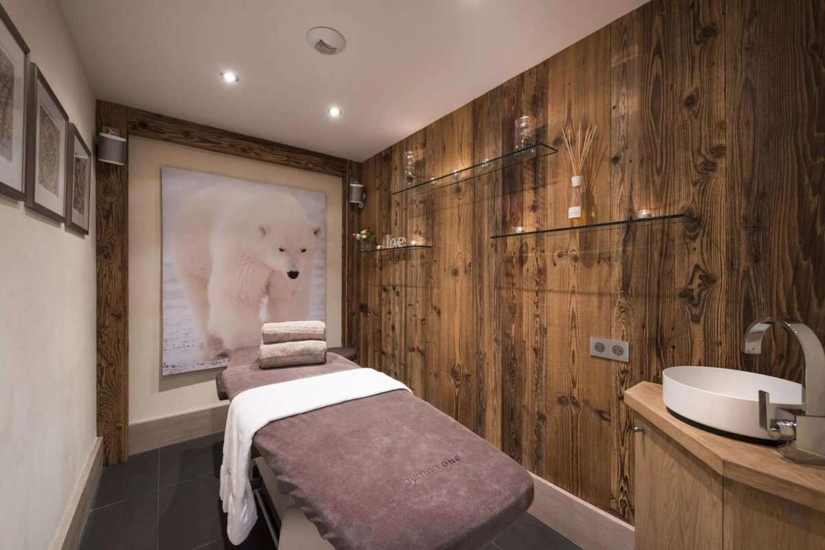 A tranquil spa room features a massage table, rich wooden walls, and a large polar bear painting, creating a cozy, natural ambiance.