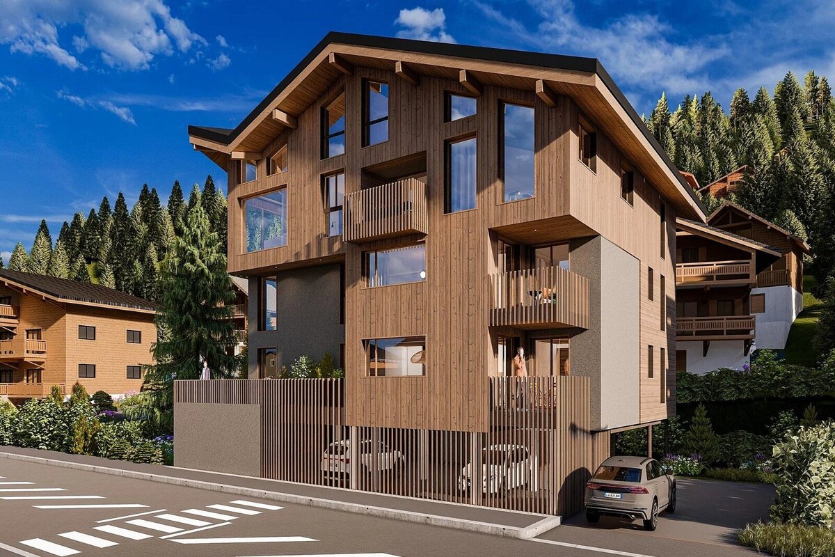 A modern wood-clad apartment building with balconies, large windows, and covered parking, set in a forested mountainscape under a blue sky.