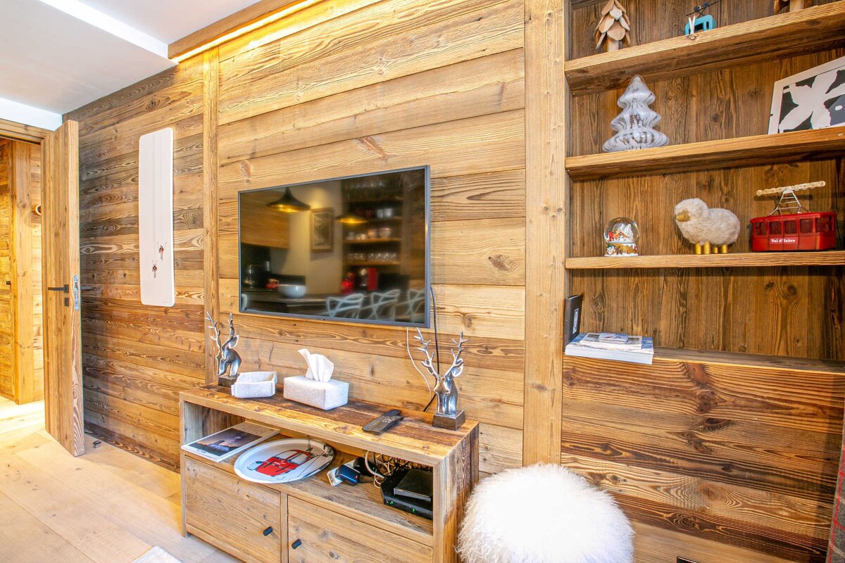 Cozy, wood-paneled living room with a TV, media console, and shelves displaying charming chalet-themed decorations.