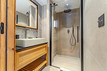 Modern bathroom featuring a wooden vanity with a white vessel sink and a glass-enclosed walk-in shower.