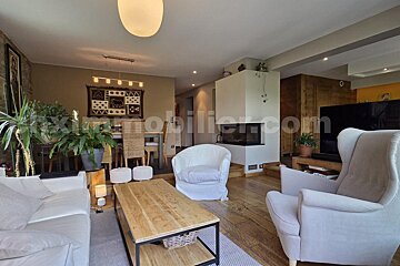 A warm, inviting open-plan living and dining room with a fireplace, white seating, wooden table, and natural accents like plants and wood flooring.