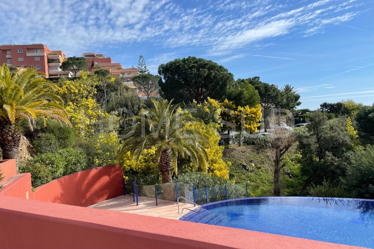 A large swimming pool is surrounded by palm trees and buildings