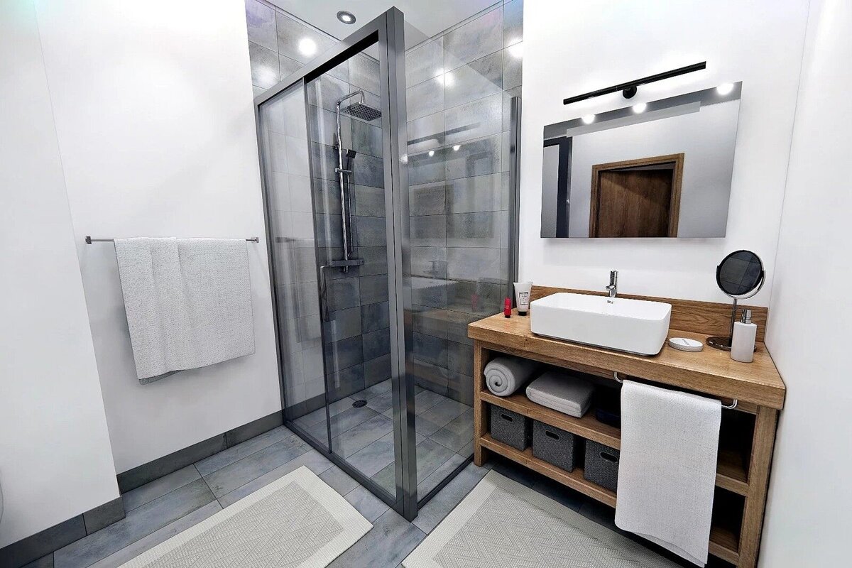 Modern bathroom with a glass shower enclosure, wooden vanity with a white vessel sink, and a mirror. Features white walls and gray tiles.