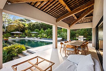 Luxury outdoor living space: a large patio with a pool, lush garden, dining table, lounge area, and an impressive wooden beamed ceiling.
