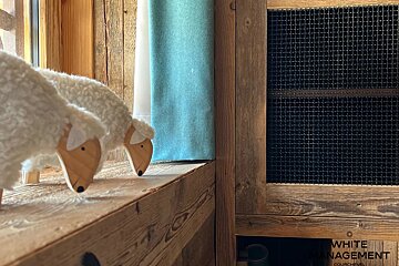Two toy sheep with wooden heads and fluffy wool stand on a rustic wooden shelf in front of a blue curtain.