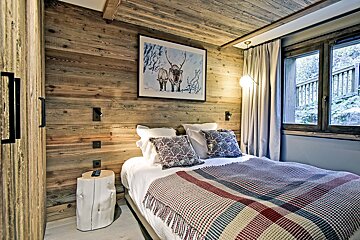 Rustic, wood-paneled bedroom with a cozy double bed, reindeer art, and a window view of nature.