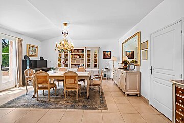 Bright, elegant dining room with a large chandelier, cane-back chairs around a table, a sideboard with a mirror, and tiled floors.