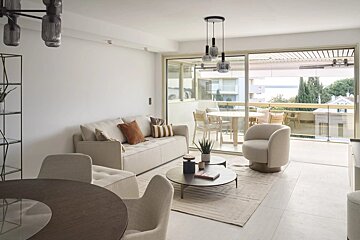 A modern, light-filled living room with neutral-toned furniture, round coffee tables, and large sliding doors opening to a balcony.