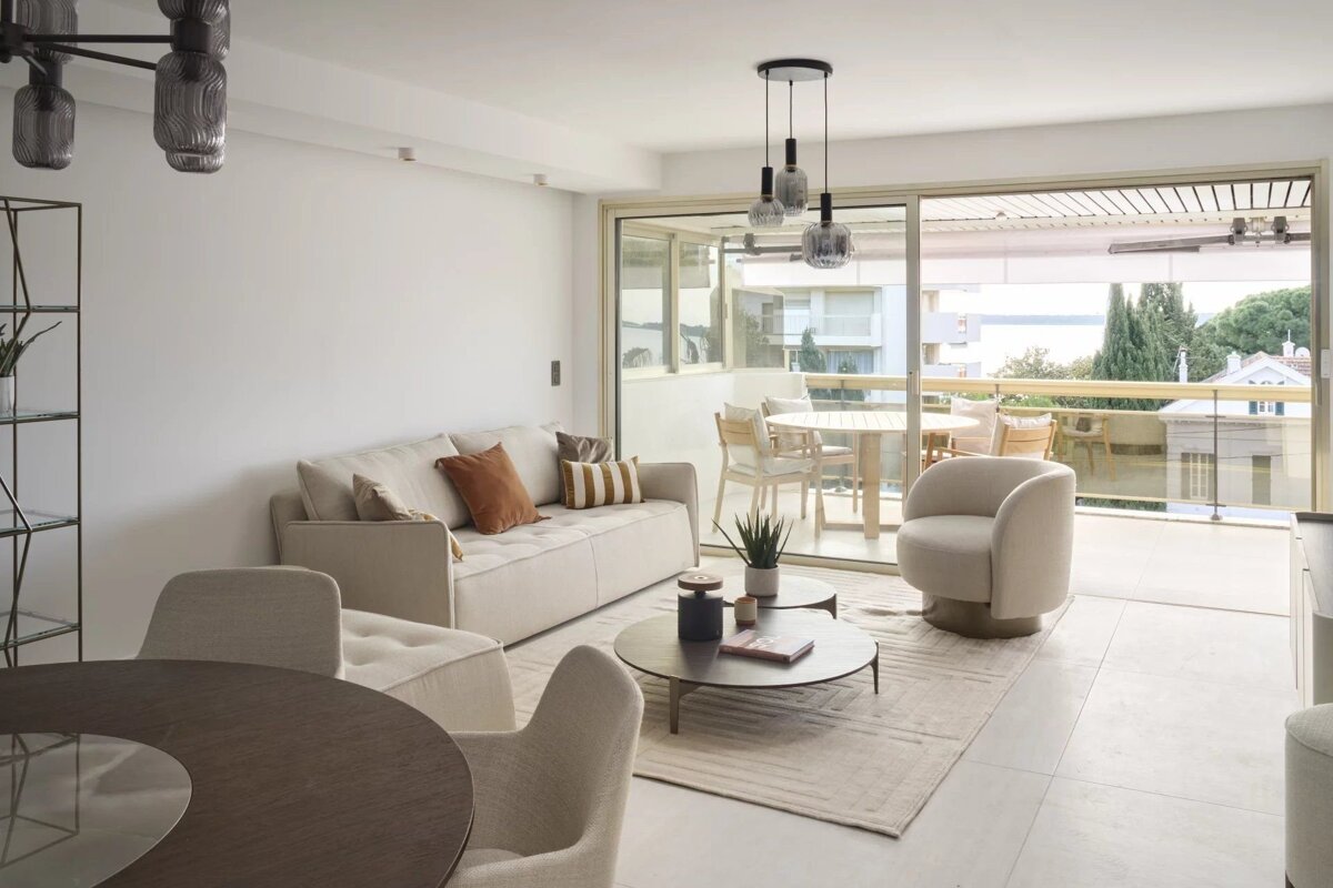 Elegant, neutral-toned living room with a beige sofa, round coffee tables, and glass doors opening to a scenic balcony.