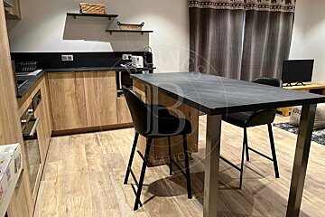 Modern wooden kitchen and dining area featuring a dark grey high-top table with two black bar stools.
