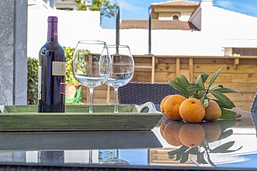 A bottle of wine sits on a table next to two wine glasses and oranges