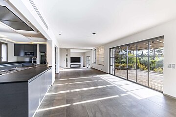 Spacious, modern open-plan living area with a sleek gray kitchen, large glass doors to a deck, and abundant natural light.