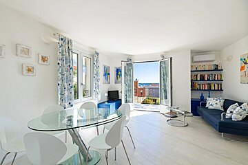 Bright, white apartment living room with blue accents, a glass dining table, and open doors leading to a balcony.