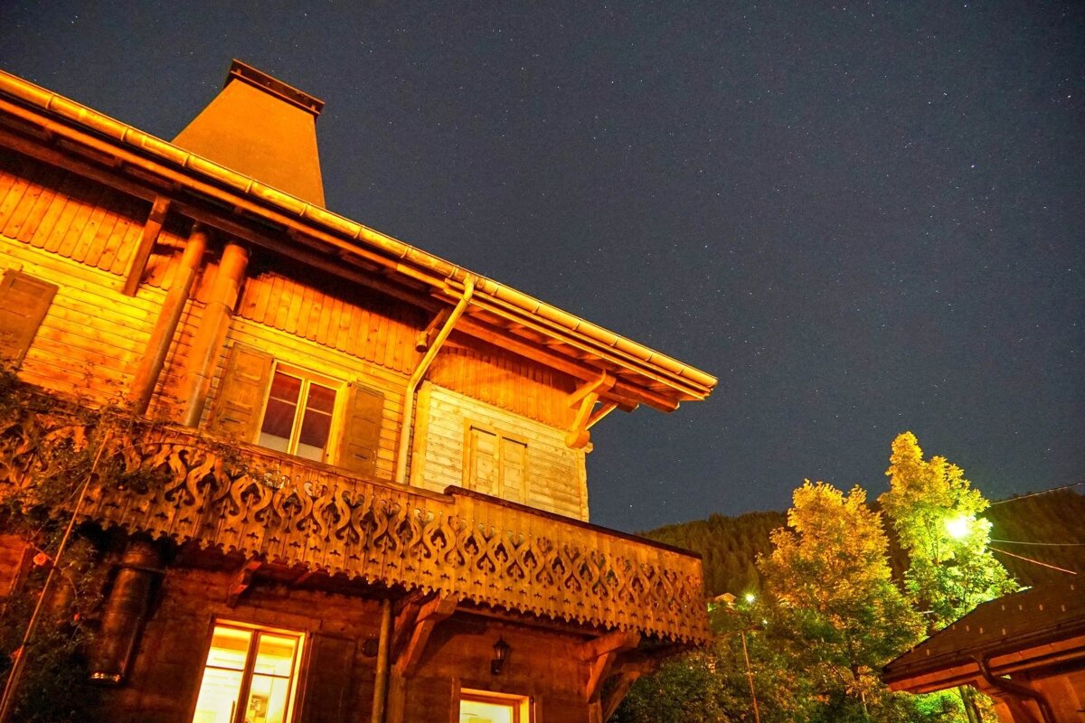 A warmly lit wooden chalet with an ornate balcony under a starry night sky.