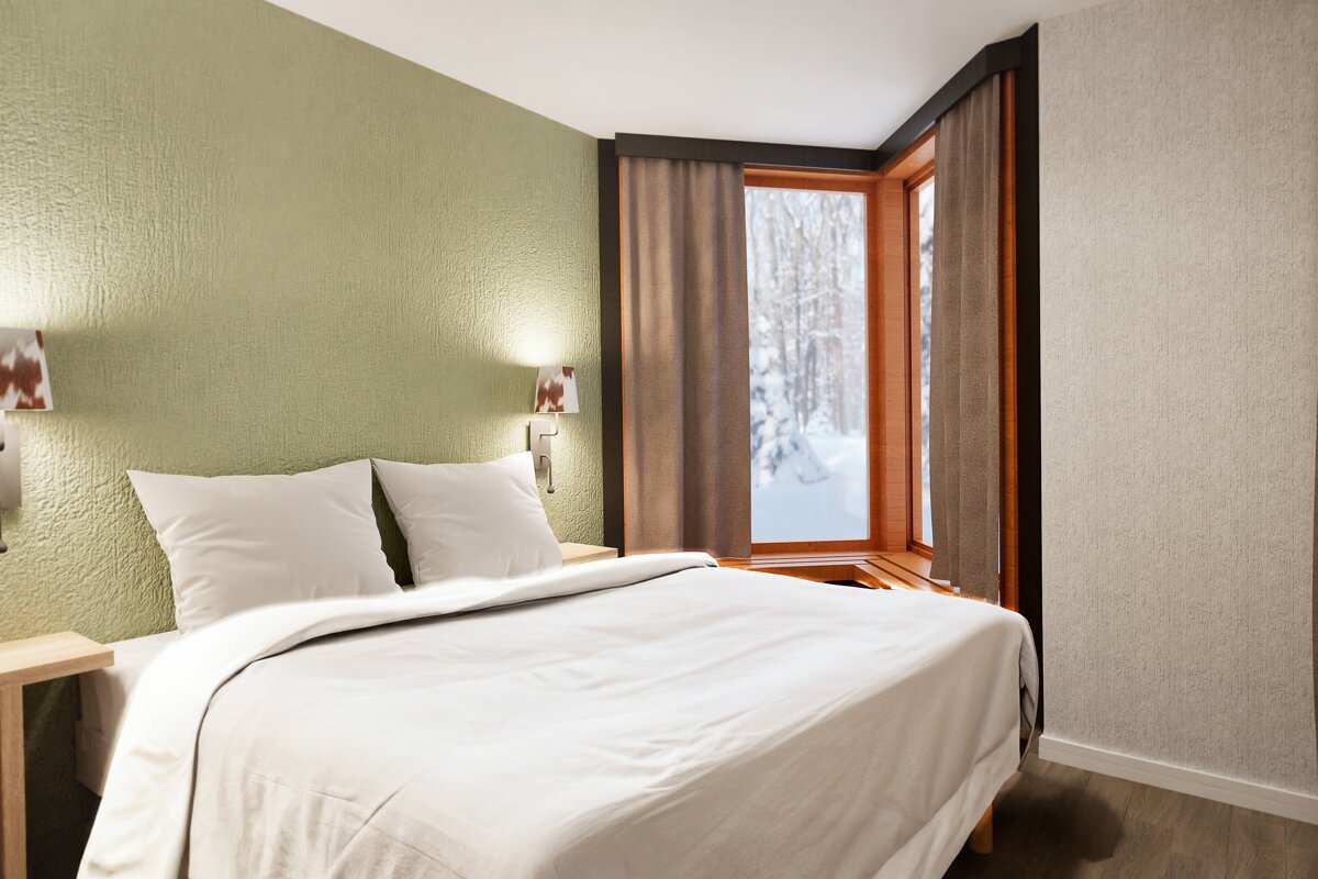 A cozy bedroom features a white bed, green textured wall, and two sconces. A large corner window overlooks a serene, snow-covered forest.