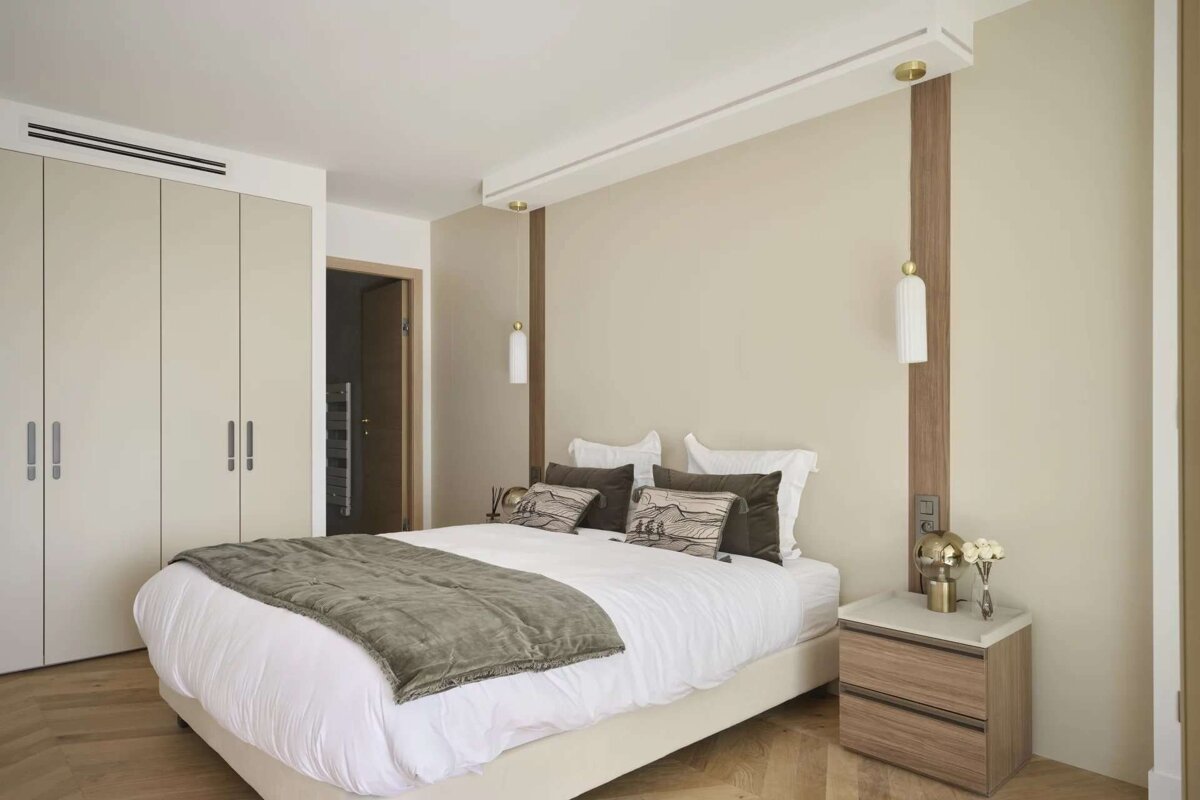 A contemporary bedroom with a large bed, neutral colors, sleek built-in closets, wood flooring, and stylish wall-mounted lamps provides a minimalist feel.