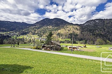 A scenic mountain valley with a small village, green fields, a road, and traditional wooden houses under a partly cloudy sky.