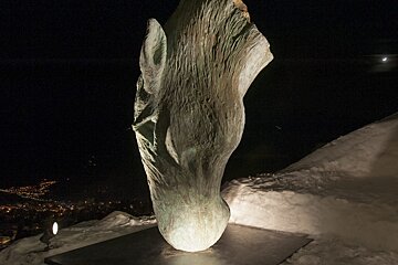 A large sculpture is lit up at night in the snow
