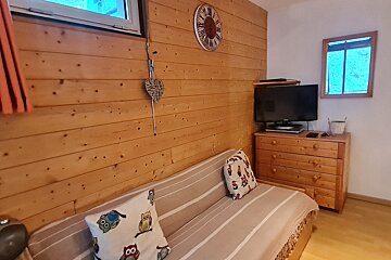 A cozy room with wood-paneled walls, a striped sofa with owl cushions, a TV on a wooden dresser, and a clock. A window is visible above.