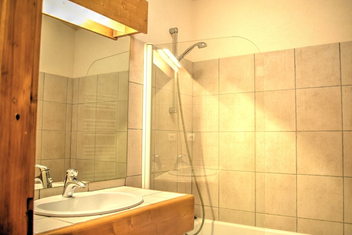 Warmly lit bathroom with a white oval sink, wooden counter, large mirror, and tiled shower with a glass screen.