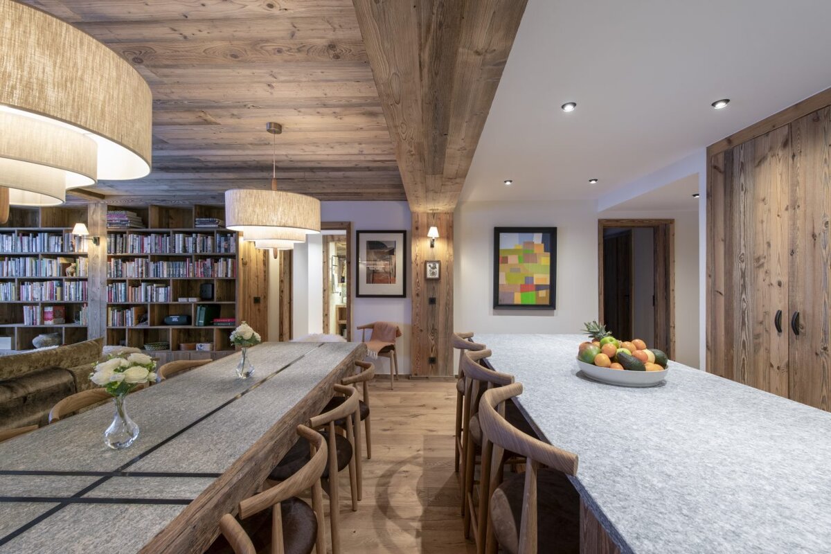 A kitchen with a long table and chairs and a bowl of fruit on the counter