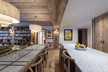 A kitchen with a long table and chairs and a bowl of fruit on the counter