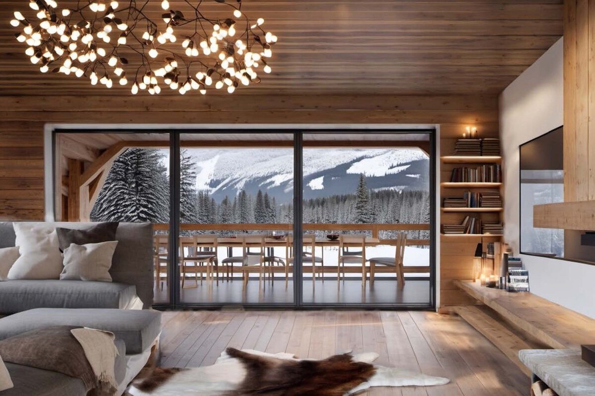 Cozy wooden chalet living room featuring a branch chandelier, plush sofa, and large sliding doors with a scenic view of snowy mountains.