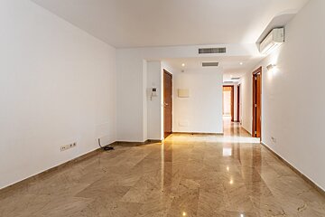 An empty, modern room with white walls, shiny beige marble floors, and dark wooden doors leading to a hallway. Features an AC unit.