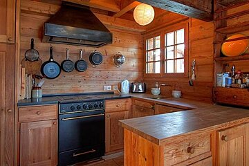 A kitchen in a log cabin with wooden cabinets and a black stove