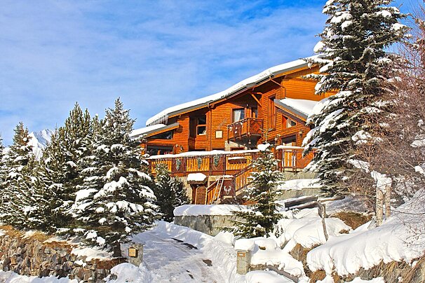 A large wooden house is surrounded by snow covered trees