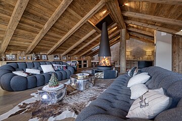 Luxurious chalet living room with vaulted wooden ceilings, a modern fireplace, grey modular sofas, and a cowhide rug, creating a cozy, upscale retreat.