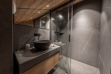 Modern bathroom featuring dark stone tiles, a wooden ceiling and vanity, a black vessel sink, and a glass walk-in shower.