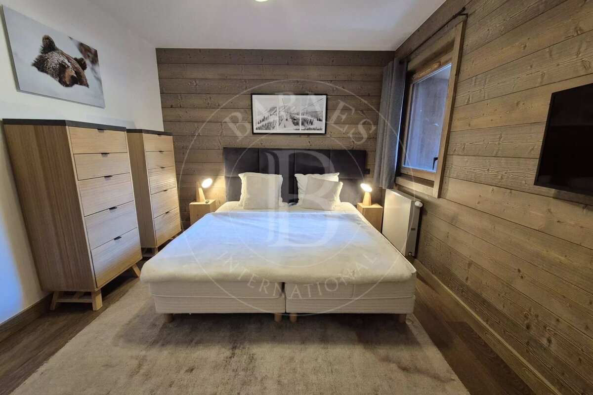 Cozy rustic bedroom with wood-paneled walls, a large bed with white bedding, two wooden dressers, and warm, inviting lighting.