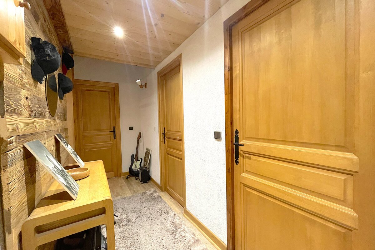A warm, wood-paneled hallway with several wooden doors, a light-colored rug, and a console table. An electric guitar stands in the background.