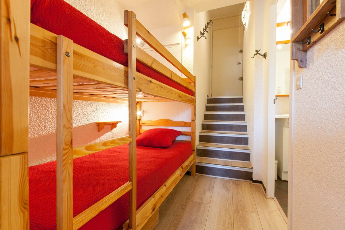 A bunk bed with red sheets is next to a set of stairs
