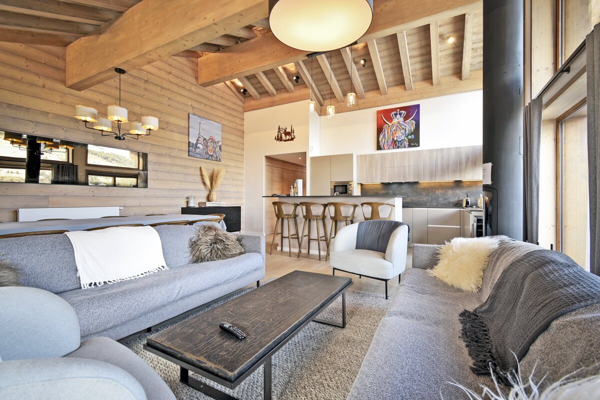 Bright, modern open-concept living space with light wood walls, vaulted ceiling, gray sofas, and a sleek kitchen with bar seating.
