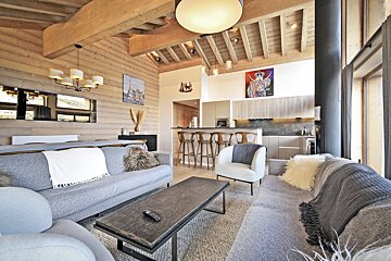 Bright, modern open-concept living space with light wood walls, vaulted ceiling, gray sofas, and a sleek kitchen with bar seating.