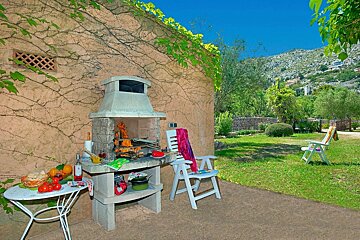 A patio area with a grill and chairs with a mountain in the background