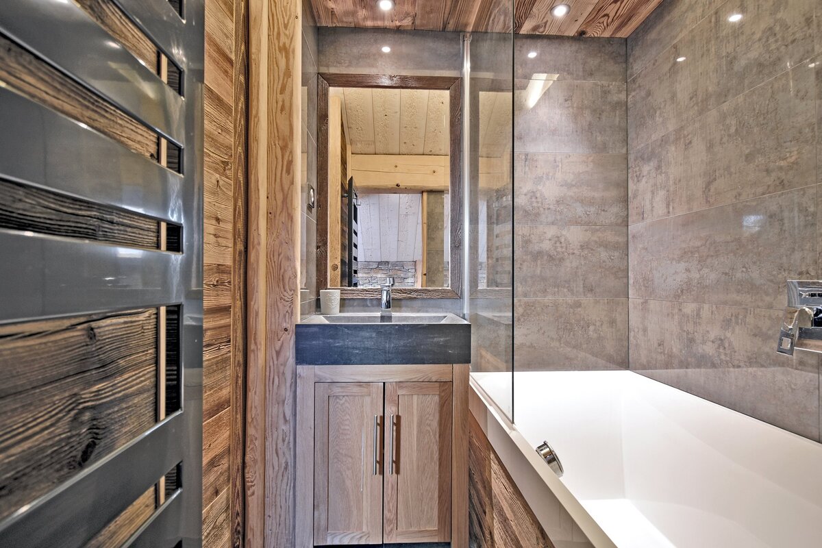 A stylish bathroom with wood walls & ceiling, gray tiled shower/bath area, and a vanity with a mirror. Modern rustic design.