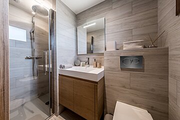 A sleek, modern bathroom with light wood-effect tiling, a walk-in shower, a floating vanity, and a hidden cistern toilet.