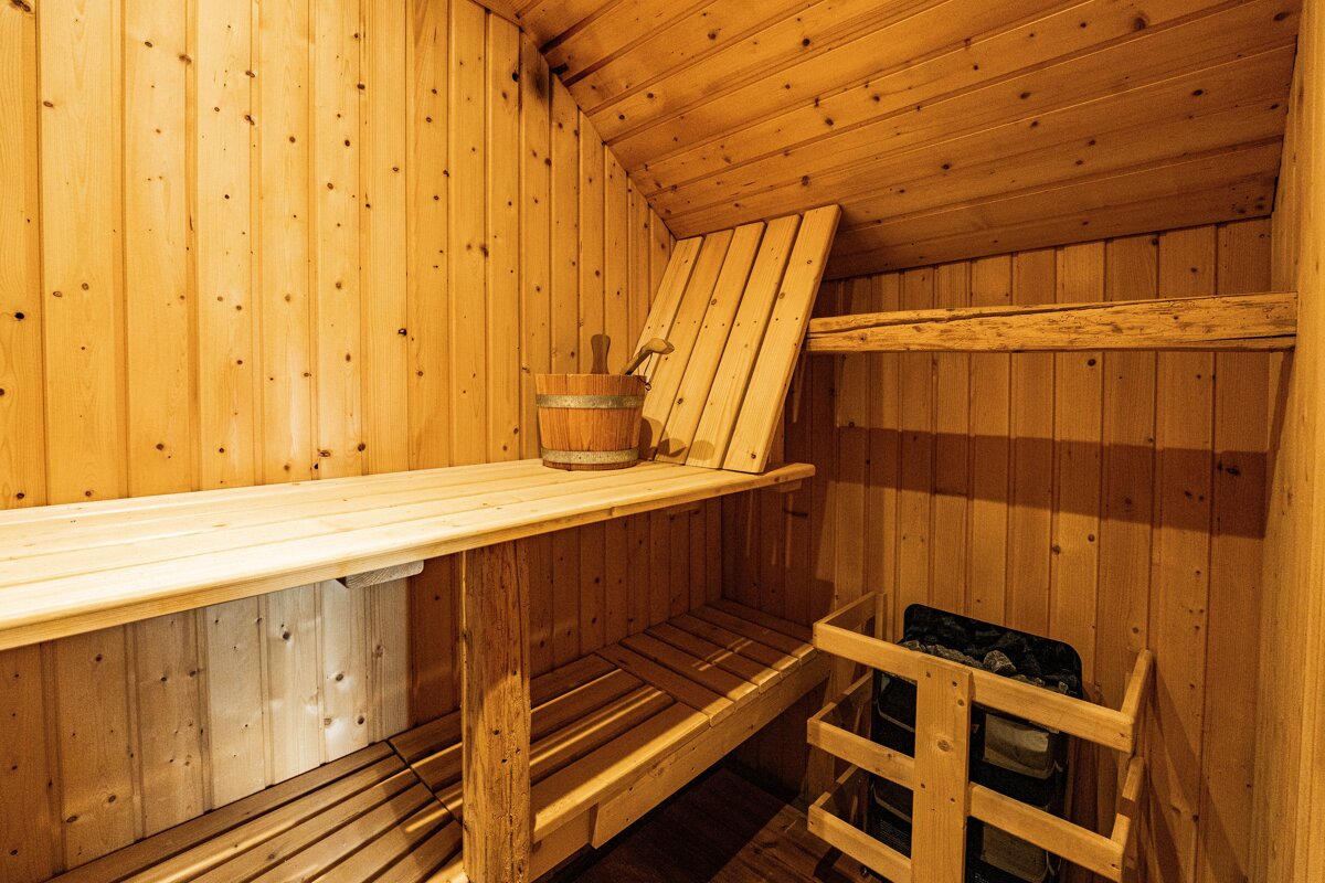 Interior of a cozy wooden sauna with multi-level benches, a bucket with a ladle, and a stone heater in the corner.