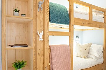 Wooden bunk beds with pink and teal blankets next to a light wood shelving unit decorated with small plants.