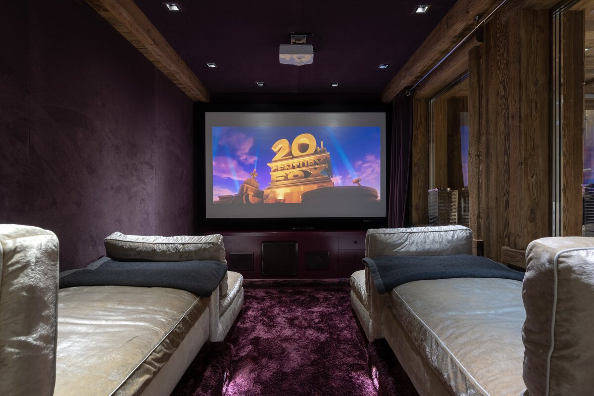 Plush home cinema with purple walls, shaggy carpet, and two loungers facing a large screen displaying the 20th Century Fox logo.
