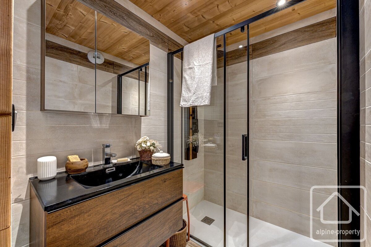 Chic bathroom with a dark wood vanity, black sink, mirrored cabinet, and glass shower. Features wooden ceiling and neutral tiles.